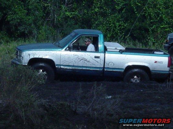Silver and teal pickup truck stuck in mud, driver visible, "Z71" badge on fender