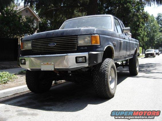Dark blue 1987 Ford F-250 pickup truck with aftermarket bumper and large tires, parked on a residential street