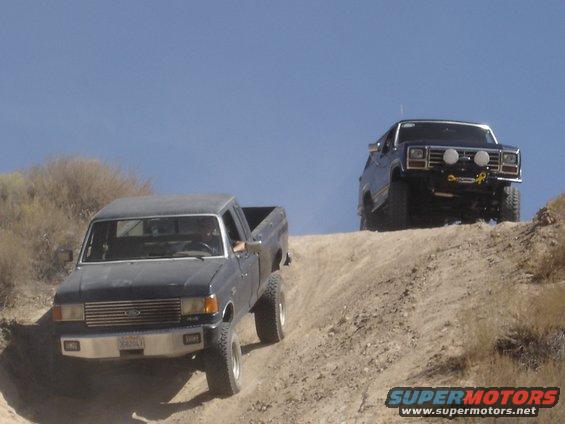 Dark gray 1987 Ford F-250 pickup truck climbing a dirt hill, another truck behind it