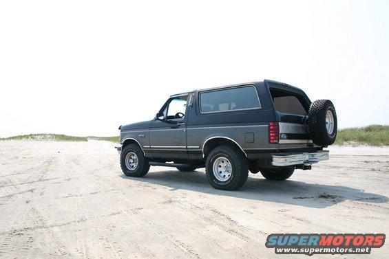 Dark gray and black Ford Bronco with a spare tire on the rear, parked on a sandy beach
