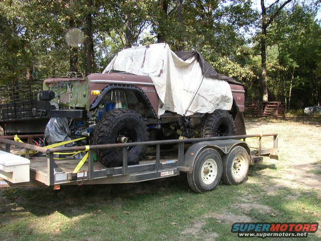 Brown 1978 Ford Bronco with large tires on a trailer, partially covered by a tarp