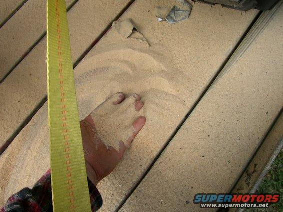 Hand reaching into sand spread on wooden planks, with a yellow strap visible