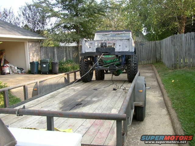 Off-road vehicle with large tires on trailer, rear view. Green differential visible