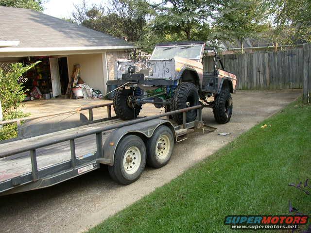 1995 Ford Bronco body being transported on a flatbed trailer, showing lifted suspension and large tires