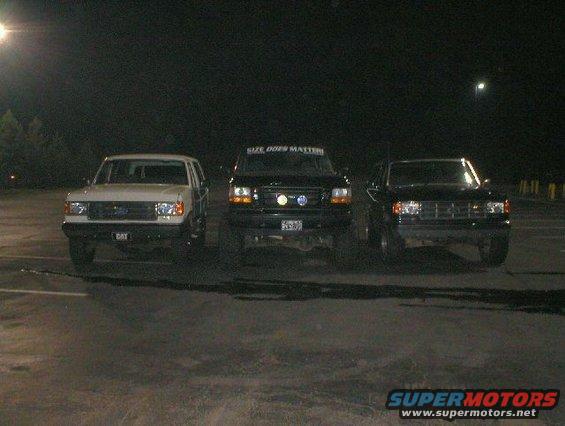 Three Ford Broncos parked in a lot at night. The middle one has 'SIZE DOES MATTER' on its windshield banner