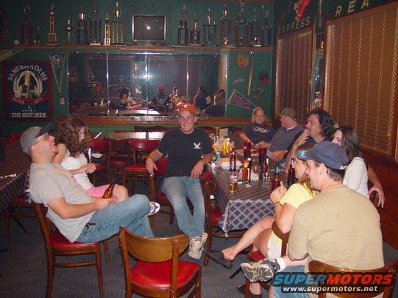 People gathered around tables in a bar with trophies on the wall