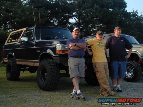 1989 Ford Bronco with lifted suspension and large tires, parked next to another truck with three men standing by