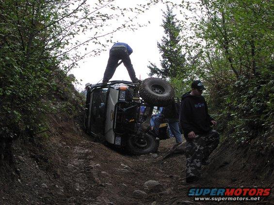 Off-road vehicle tipped on its side on a dirt trail with people around it