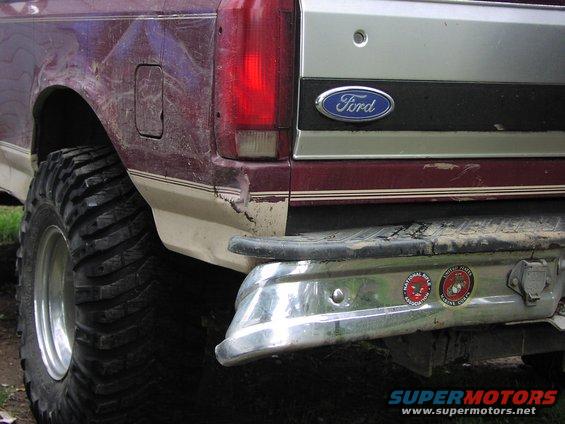 Maroon and tan Ford Bronco rear quarter panel with large off-road tires and chrome bumper. Dented and scratched