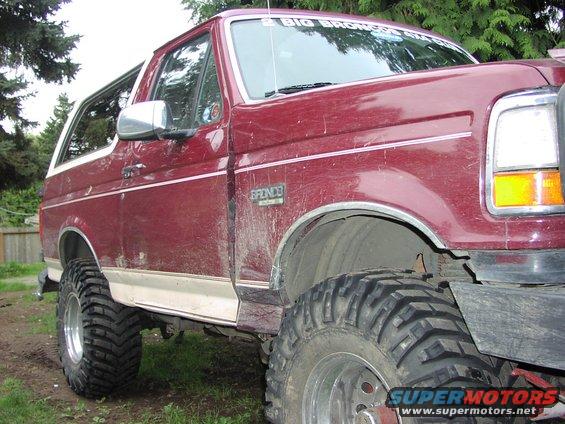 Maroon Ford Bronco with lifted suspension and large tires. "BIG BRONCOS STUFF" sticker on windshield
