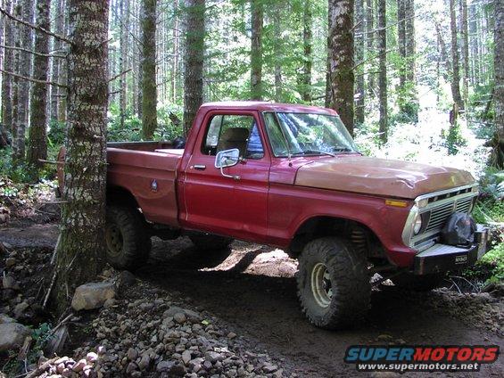 Red pickup truck with a brown hood, off-roading in a forest