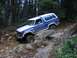 1993 Ford Bronco - A blue and white Ford Bronco tackles a challenging rocky path in a wooded area.