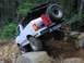 1993 Ford Bronco - White 1993 Ford Bronco navigates a challenging rocky off-road course in a wooded area.