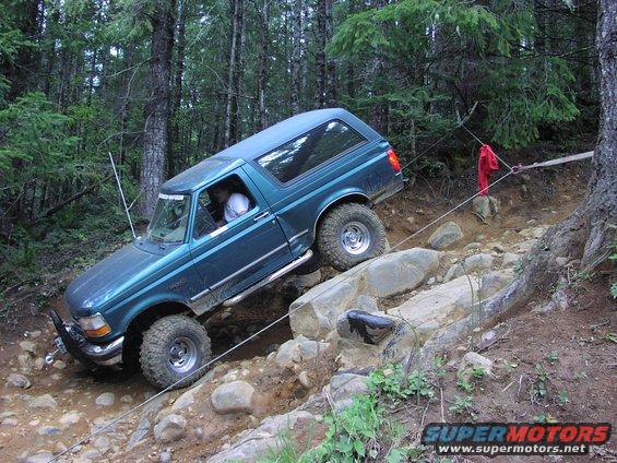 Teal 1993 Ford Bronco climbing over rocks on a wooded trail