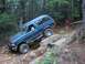 1993 Ford Bronco - A teal 1993 Ford Bronco navigates a challenging rocky obstacle on an off-road trail.