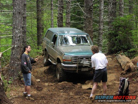 Green Ford Bronco off-roading, front winch attached to a rope, two people present
