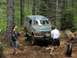1993 Ford Bronco - A green Ford Bronco navigates a challenging off-road trail with two individuals assisting.