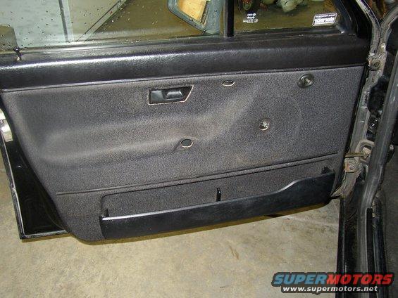 Interior of a car door panel with fabric upholstery, a pull handle, and a storage pocket