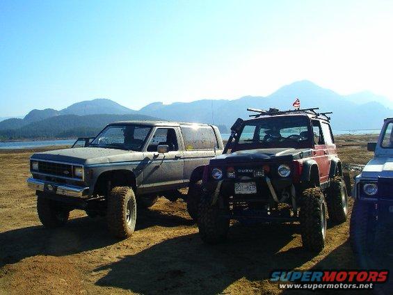 Two modified SUVs parked on a sandy beach with mountains in the background
