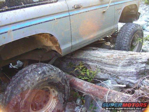 Side view of a light blue Ford Bronco with blue trim, tires are large and knobby, vehicle is on logs and rocks
