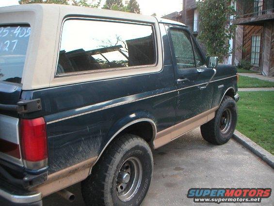 Dark green and tan Ford Bronco, rear quarter panel and side visible, dusty condition
