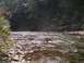 1994 Ford Bronco - A sun-dappled river flows over rocks, bordered by trees. The Supermotors.net logo is visible in the lower right corner.
