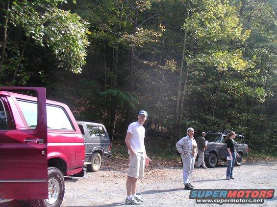 Two Ford Bronco SUVs parked on a dirt road with people standing nearby