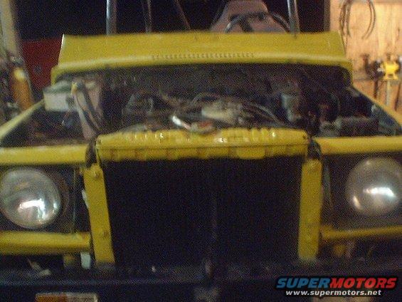 Yellow SUV front with hood open, showing engine and radiator. Round headlights visible