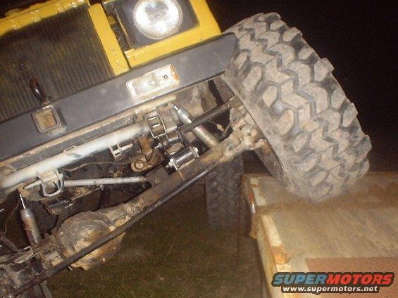 Off-road vehicle front suspension, large tire, and part of yellow body. Tire is on a trailer
