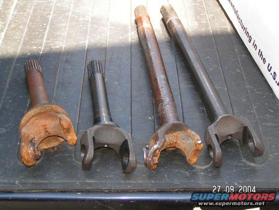 Four drive shafts, two rusty and two clean, laid out on a dark surface