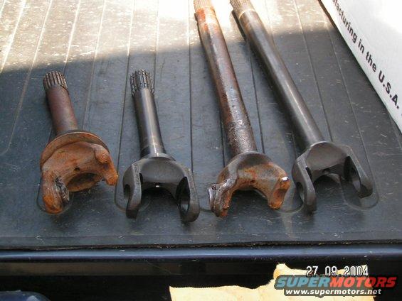 Four driveshaft yokes and shafts, two rusty and two clean, laid out on a dark surface