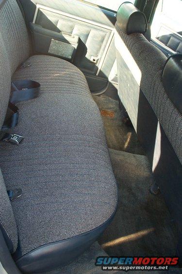 Car interior showing rear bench seat and door panel. Dark fabric seats and carpet. Water stains on carpet