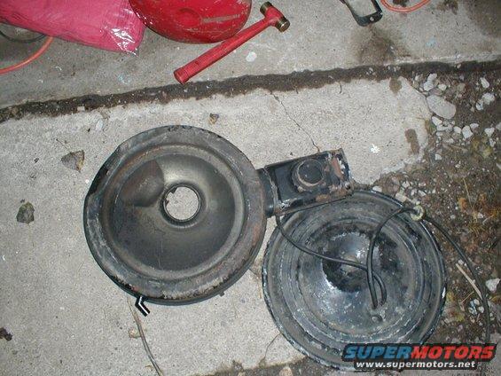 Two parts of an air cleaner assembly are on the ground next to a red hammer and a red bag