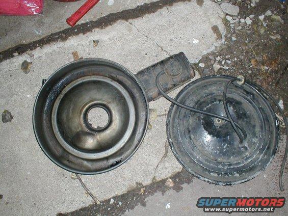 Air cleaner assembly with a metal base and a black lid, lying on concrete