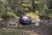 1994 Ford Bronco - A red SUV navigates a shallow, rocky stream bed surrounded by trees.