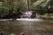 1994 Ford Bronco - A red SUV navigates a shallow creek bed surrounded by dense woods.