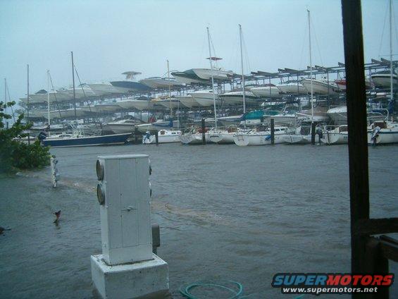 Many boats are stored on racks in a marina with choppy water, suggesting stormy weather