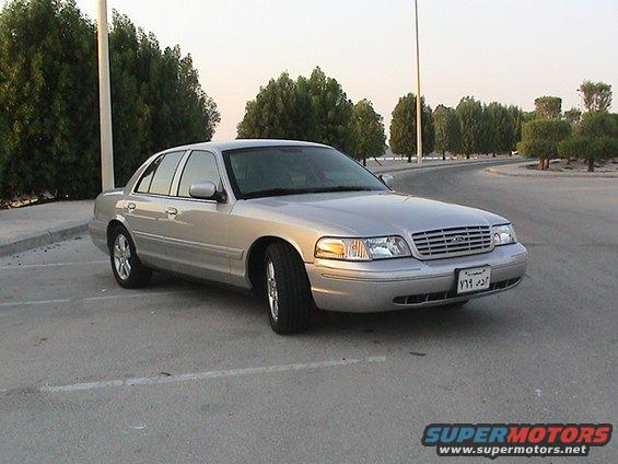 Silver 2004 Ford Crown Victoria parked on asphalt with trees and a body of water in the background