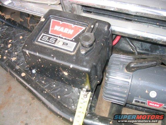 Black Warn 9.5P winch mounted on a dirty vehicle bumper with a tape measure nearby