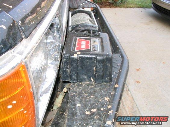 Close-up of a Warn winch mounted on a vehicle's front bumper, next to the headlight