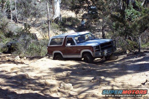 Ford Bronco navigating a rocky, off-road trail. Another vehicle is visible in the background