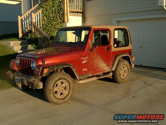 Red Jeep Wrangler with tan top, covered in mud splashes, parked in a driveway