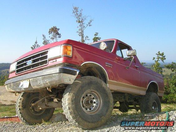 Red Ford Bronco with lifted suspension and large tires, viewed from a low front 3/4 angle