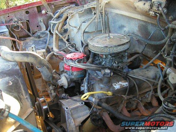 Engine bay of a Ford vehicle, showing carburetor, distributor, and exhaust manifold