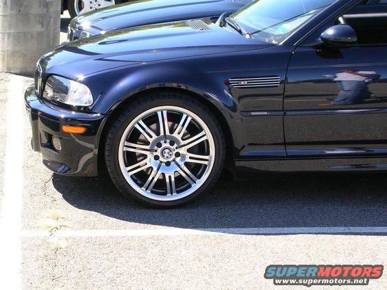 Dark blue BMW M3 front fender, headlight, and alloy wheel. Another car is parked behind it