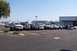 1990 Ford Bronco - A line of trucks and SUVs are parked in a lot on a clear day, with a store in the background.