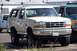 1990 Ford Bronco - A tan 1990 Ford Bronco with a cracked windshield and visible damage to its side is parked next to another vehicle.