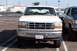 1990 Ford Bronco - A white Ford Bronco with a cracked windshield is parked next to a green SUV in a parking lot.