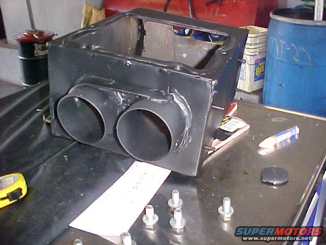 Black metal custom exhaust component with dual pipes on a workbench