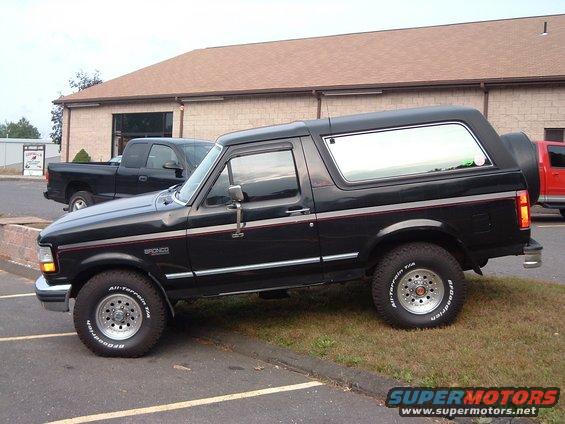 Black 1993 Ford Bronco parked on grass next to a black pickup truck